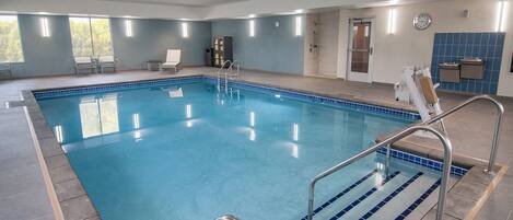 A large indoor swimming pool with clear blue water, surrounded by tiled walls and a door leading to a changing room.