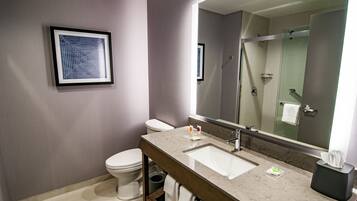 A modern bathroom with a marble sink, a framed artwork, a toilet, and a glass shower enclosure.