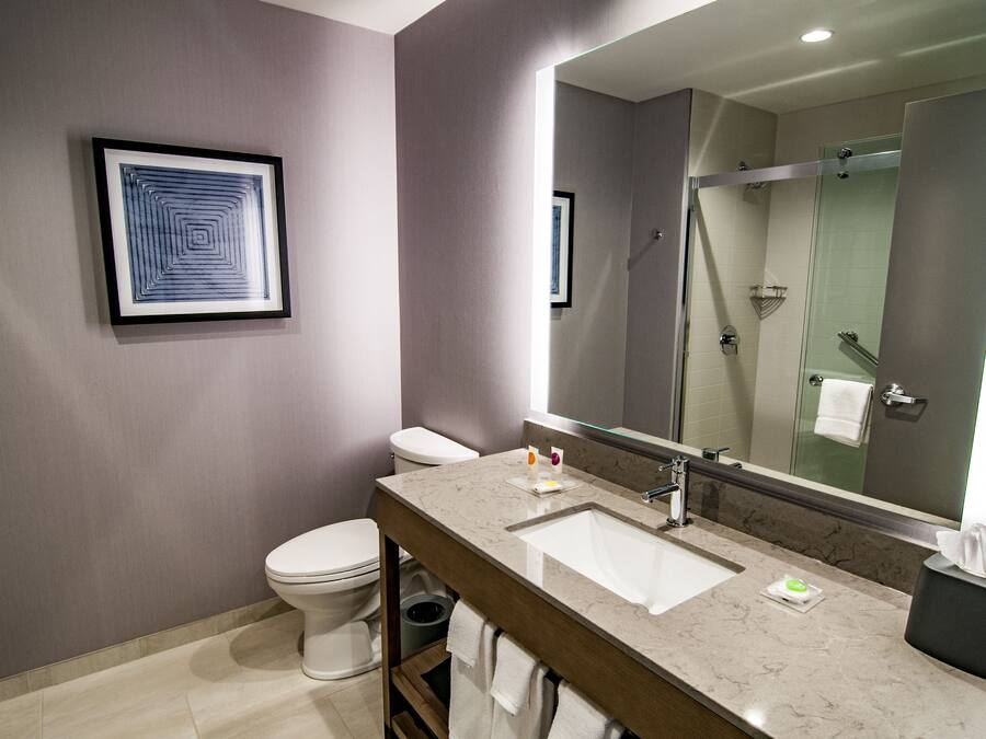 A modern bathroom with a marble sink, a framed artwork, a toilet, and a glass shower enclosure.
