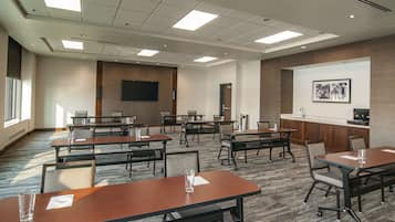 A conference room with multiple tables and chairs, a flat-screen TV mounted on the wall, and a framed artwork above the counter.