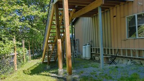 A wooden structure with a ladder, a metal fence, and a building with a window and gas cylinders. - 2 PERSON - 1 BEDROOM PRIVATE RENTAL ABOVE GOLDSTREAM PROVINCIAL PARK (Victoria)
