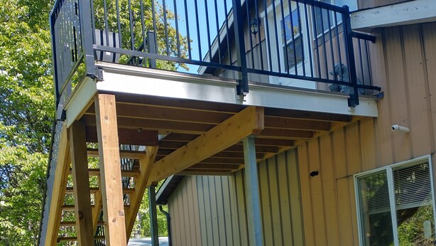 A wooden deck with a metal railing, a ladder, and a window overlooking a grassy area. - 2 PERSON - 1 BEDROOM PRIVATE RENTAL ABOVE GOLDSTREAM PROVINCIAL PARK (Victoria)