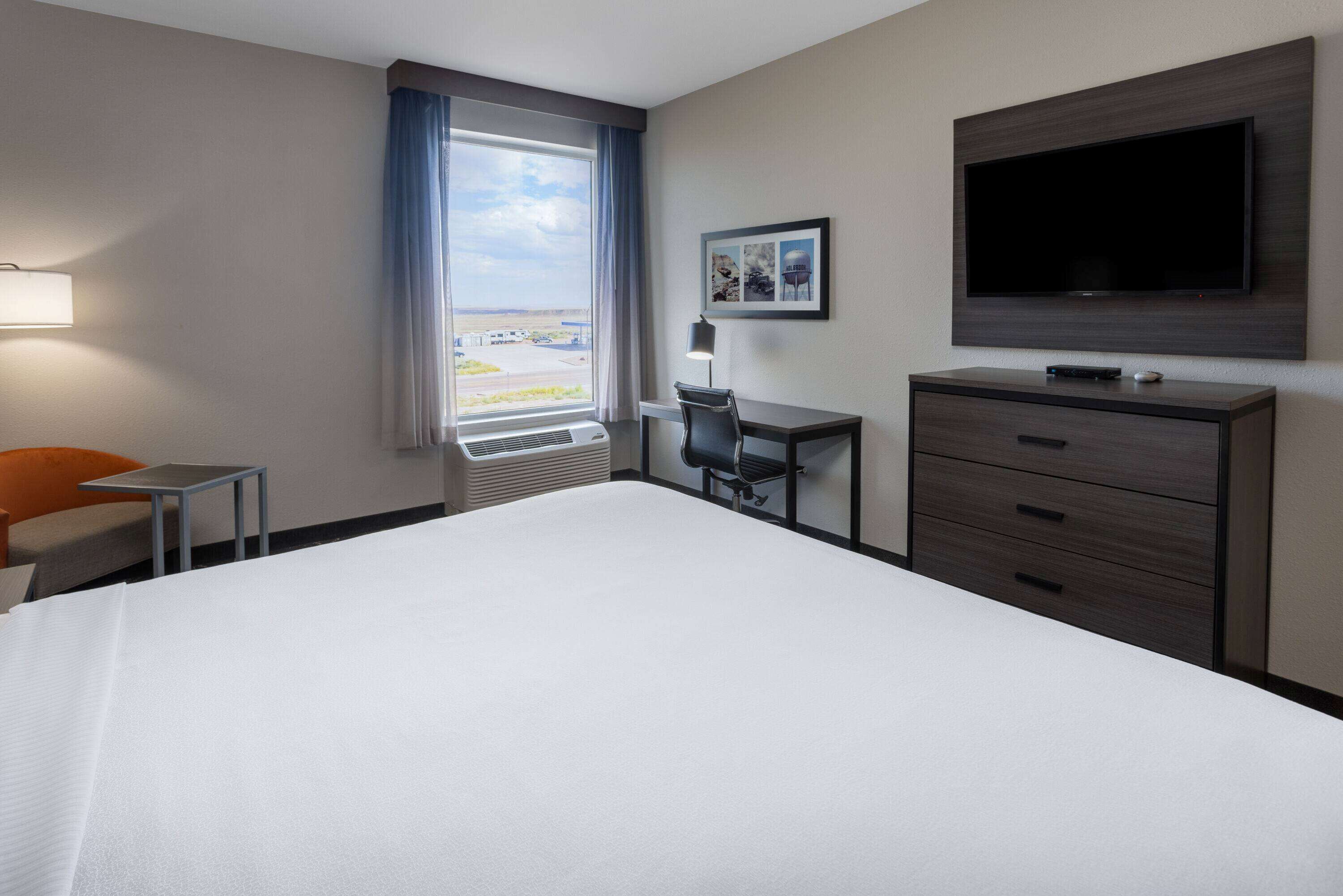 Une chambre d’hôtel avec un grand lit, un bureau, une chaise, une télévision et une fenêtre donnant sur un beau paysage.