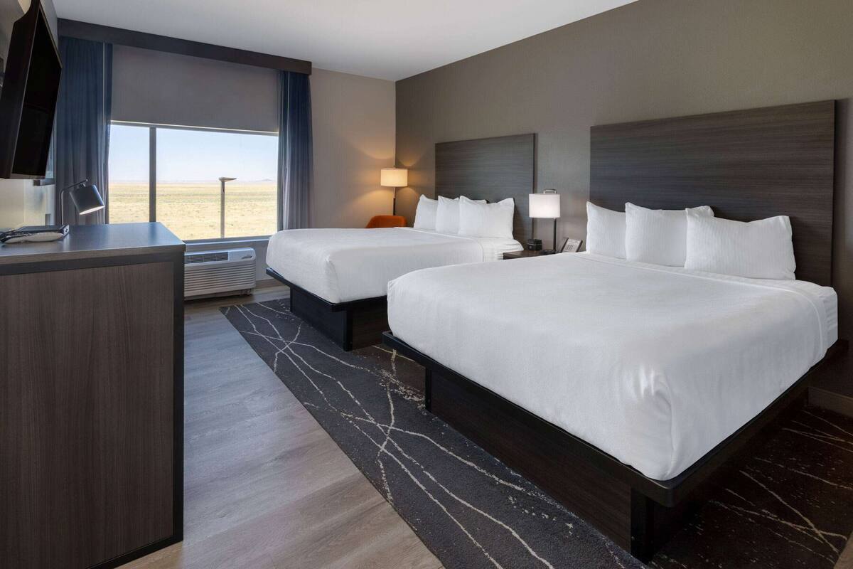 Hotelkamer met twee bedden, een bureau en een groot raam met uitzicht op de woestijn.