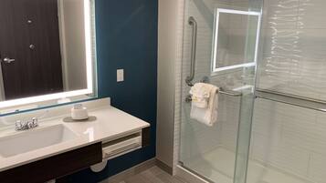 A modern bathroom with a glass-enclosed shower, a white sink with a large mirror, and a dark blue accent wall.