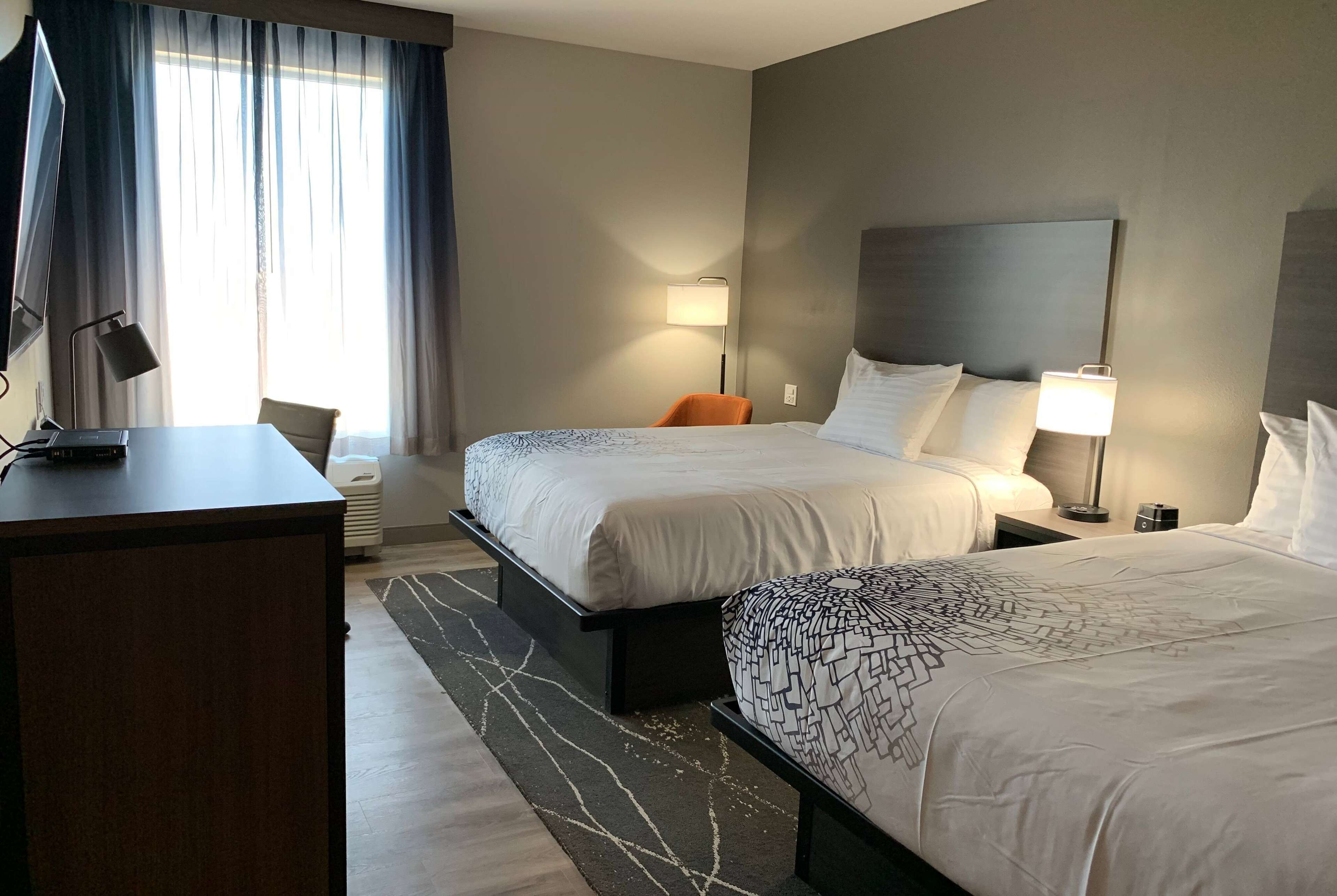 Ein Hotelzimmer mit zwei Betten, einem Schreibtisch, einem Stuhl und einem Fernseher.