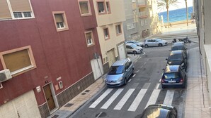 A street view with parked cars, a pedestrian crossing, and buildings with balconies overlooking a beach. - Apartment 10 meters from the beach (Almería)