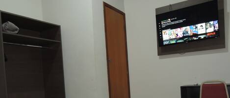 A hotel room with a bed, a TV mounted on the wall, a wardrobe, and a desk with a chair.