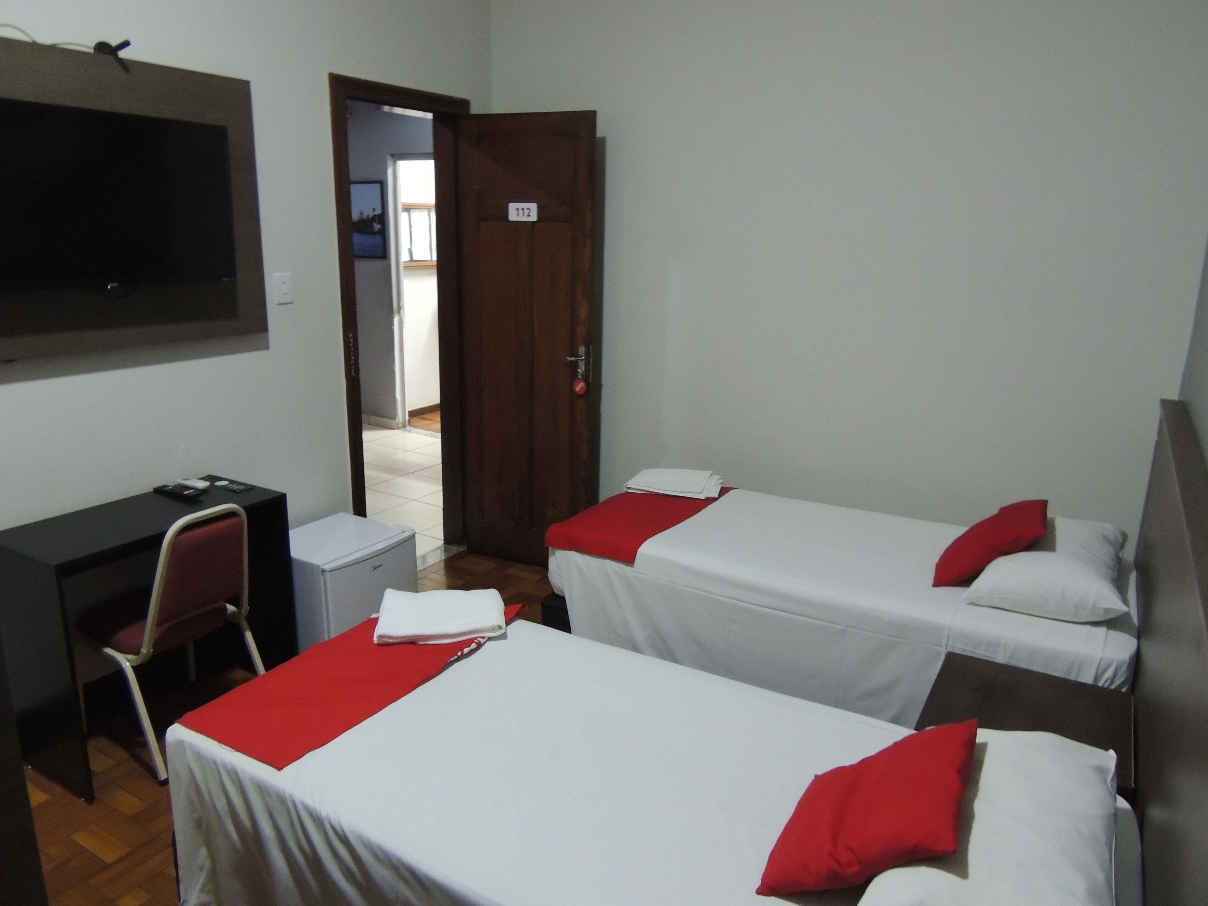 Une chambre d’hôtel avec deux lits simples, un bureau avec une chaise, une télévision et une porte donnant sur un balcon.