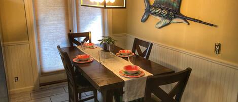 Ein Esszimmer mit einem Holztisch, gedeckt für vier Personen, einer hängenden Leuchte und einem dekorativen Fisch-Wandbild.