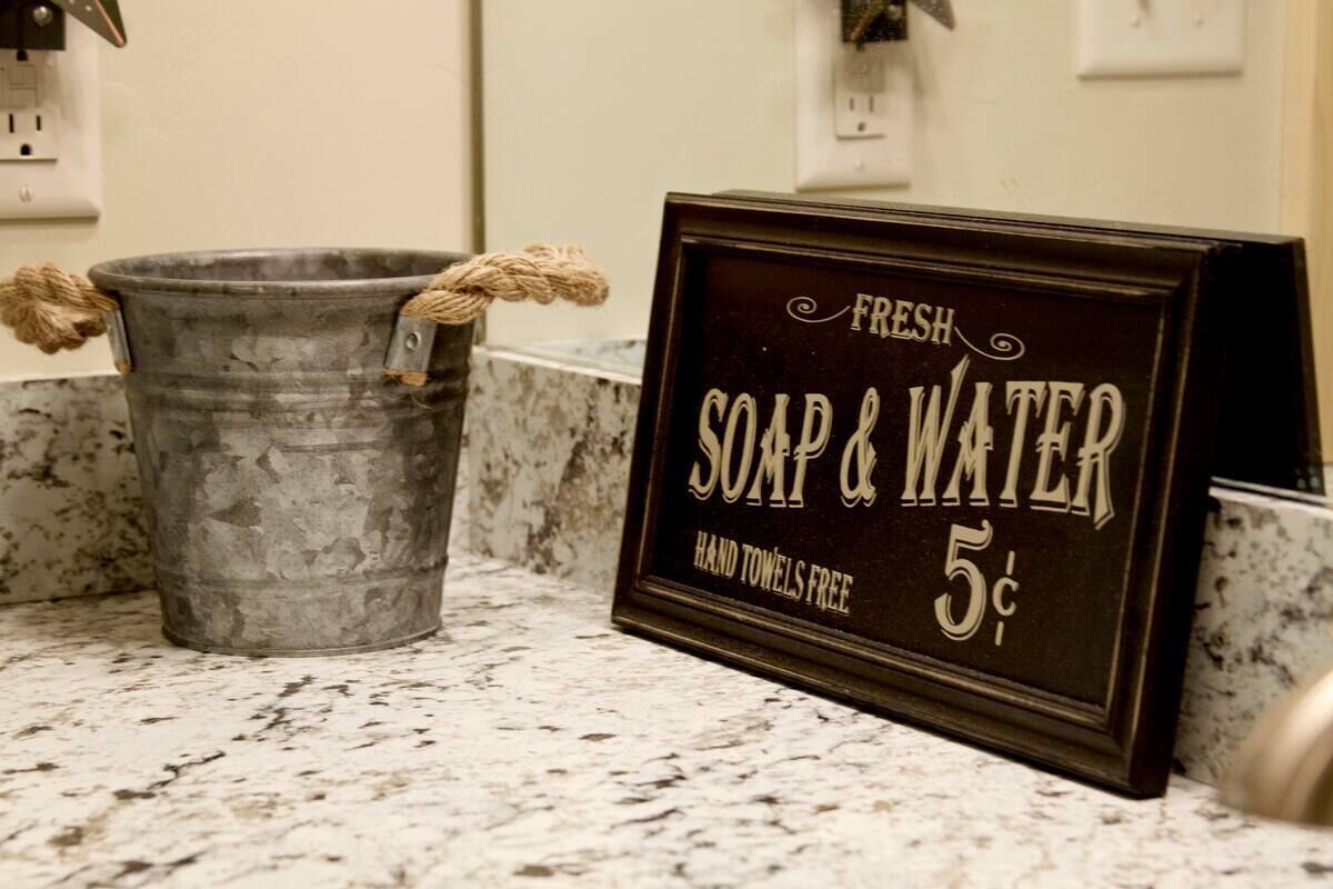 A metal bucket with rope handles and a sign offering fresh soap and water for 5 cents, hand towels included.