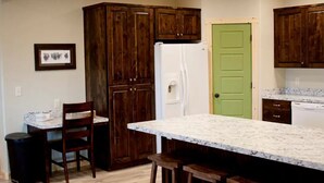 A kitchen with dark wooden cabinets, a white refrigerator, a green door, and a marble countertop. - Main Street apt. with theater room near West Yellowstone and the Tetons (Ashton)