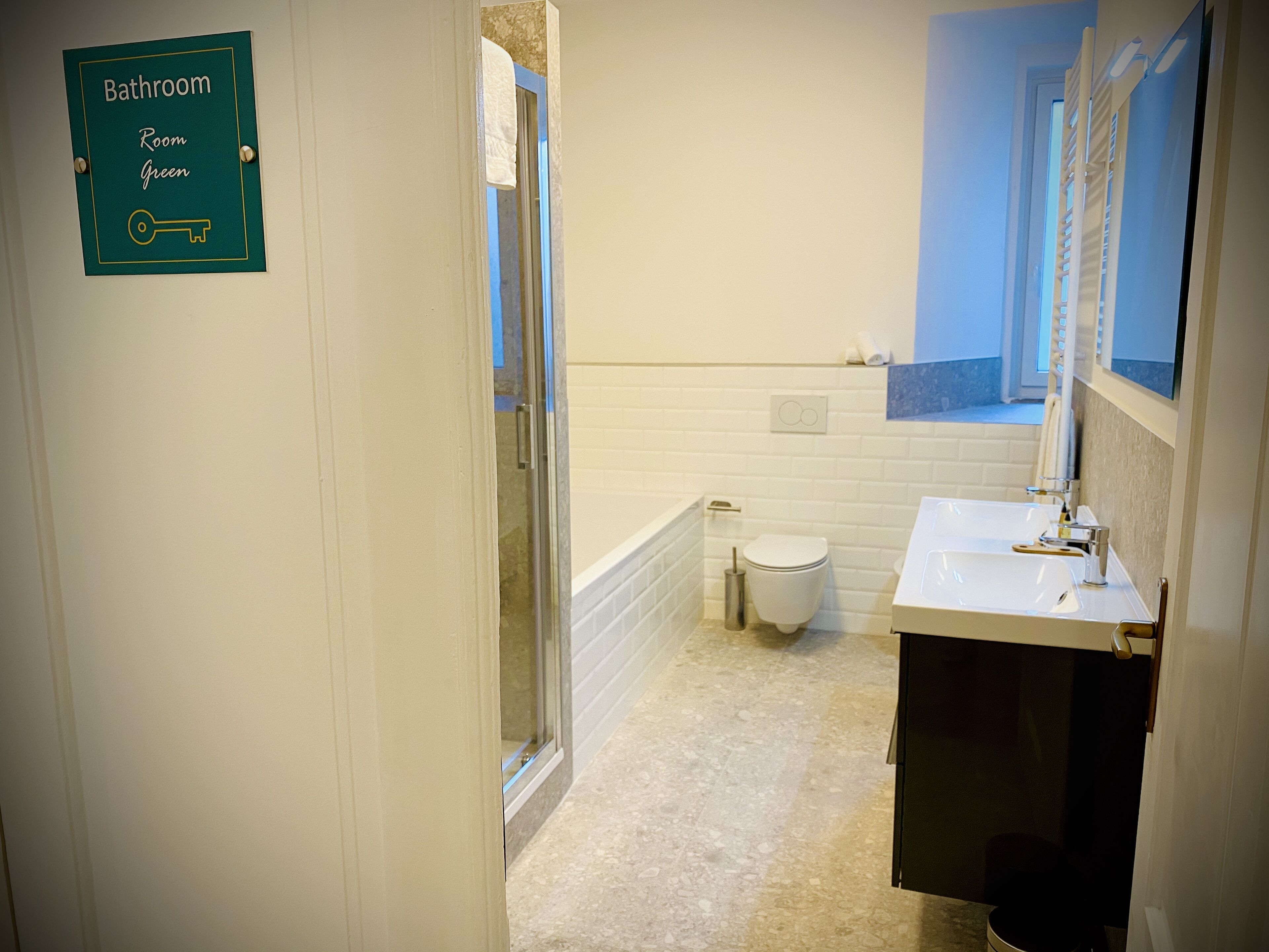 Baño con inodoro, lavamanos y bañera. Un letrero indica que el baño está en la Habitación Verde.