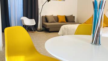 Una sala de estar moderna con una mesa redonda blanca, sillas amarillas, un sofá con cojines amarillos y marrones, una lámpara de pie y un cuadro en la pared.