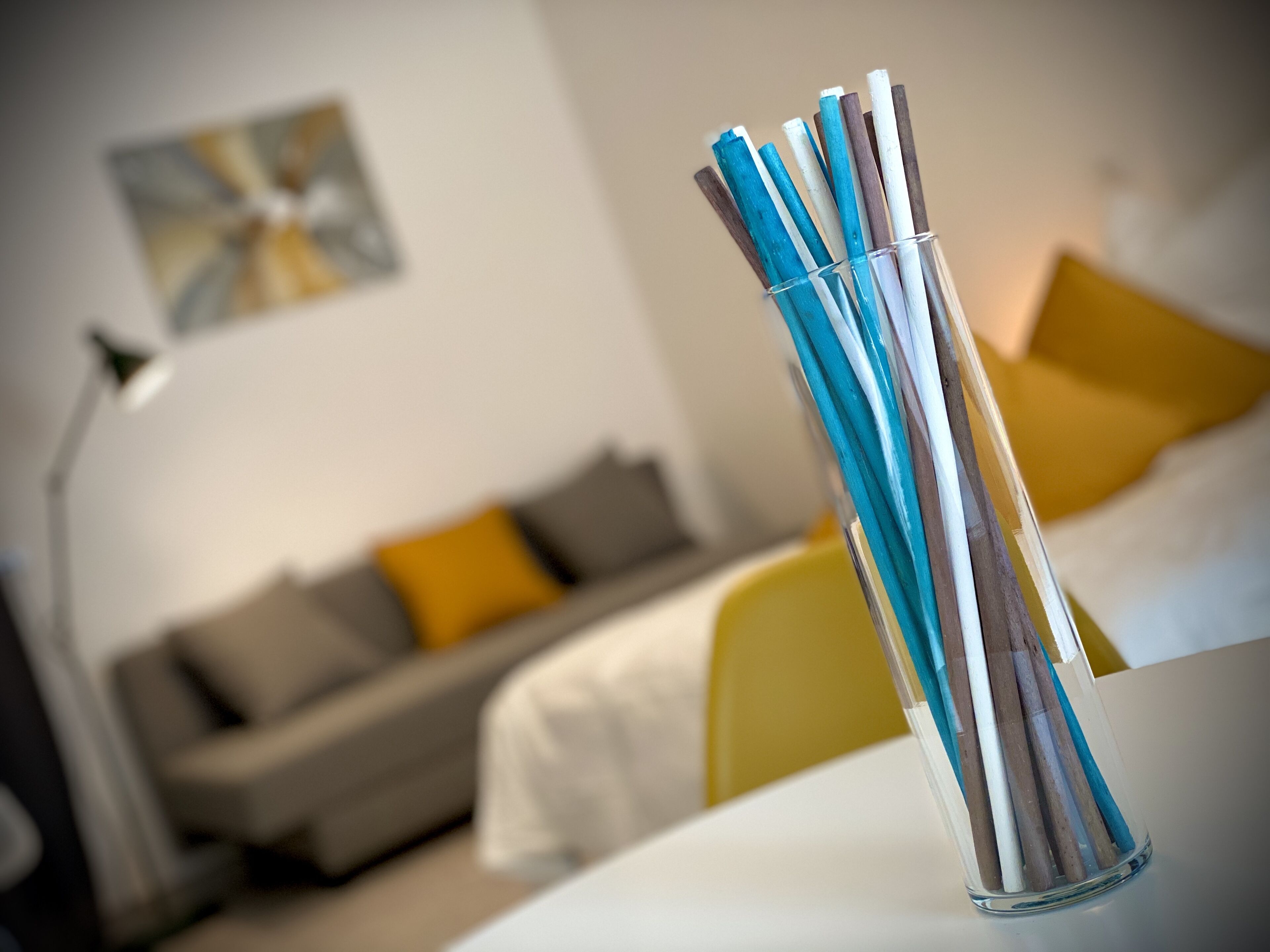 Una habitación con una cama, un sofá y un florero de vidrio con lápices.