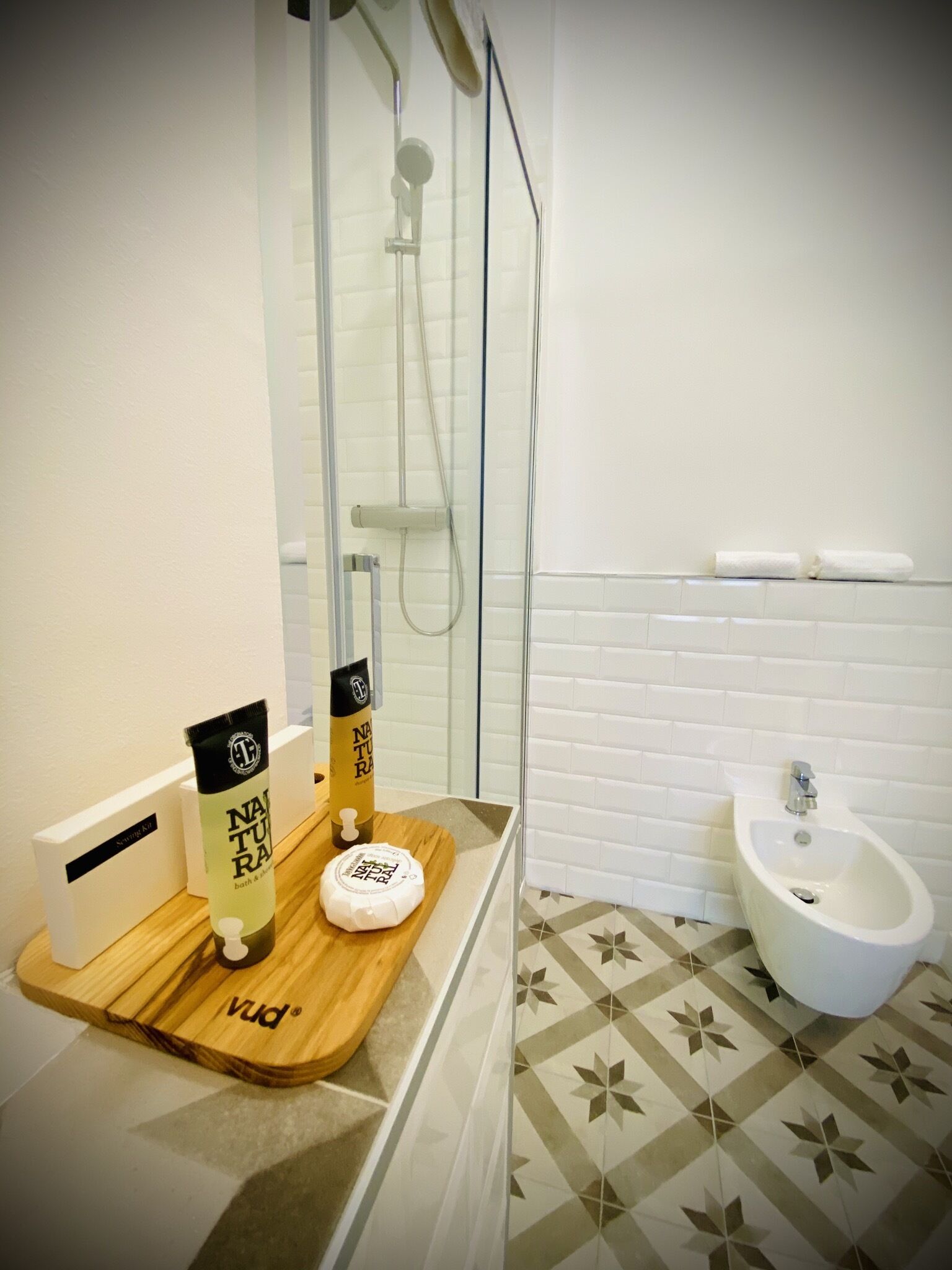 Un baño con ducha, un bidé y un mueble de tocador de madera con artículos de aseo.