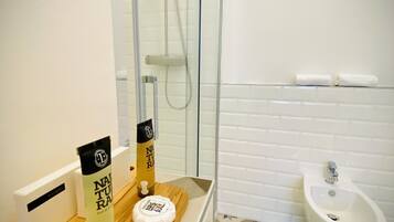 Un baño con ducha, un bidé y un mueble de tocador de madera con artículos de aseo.