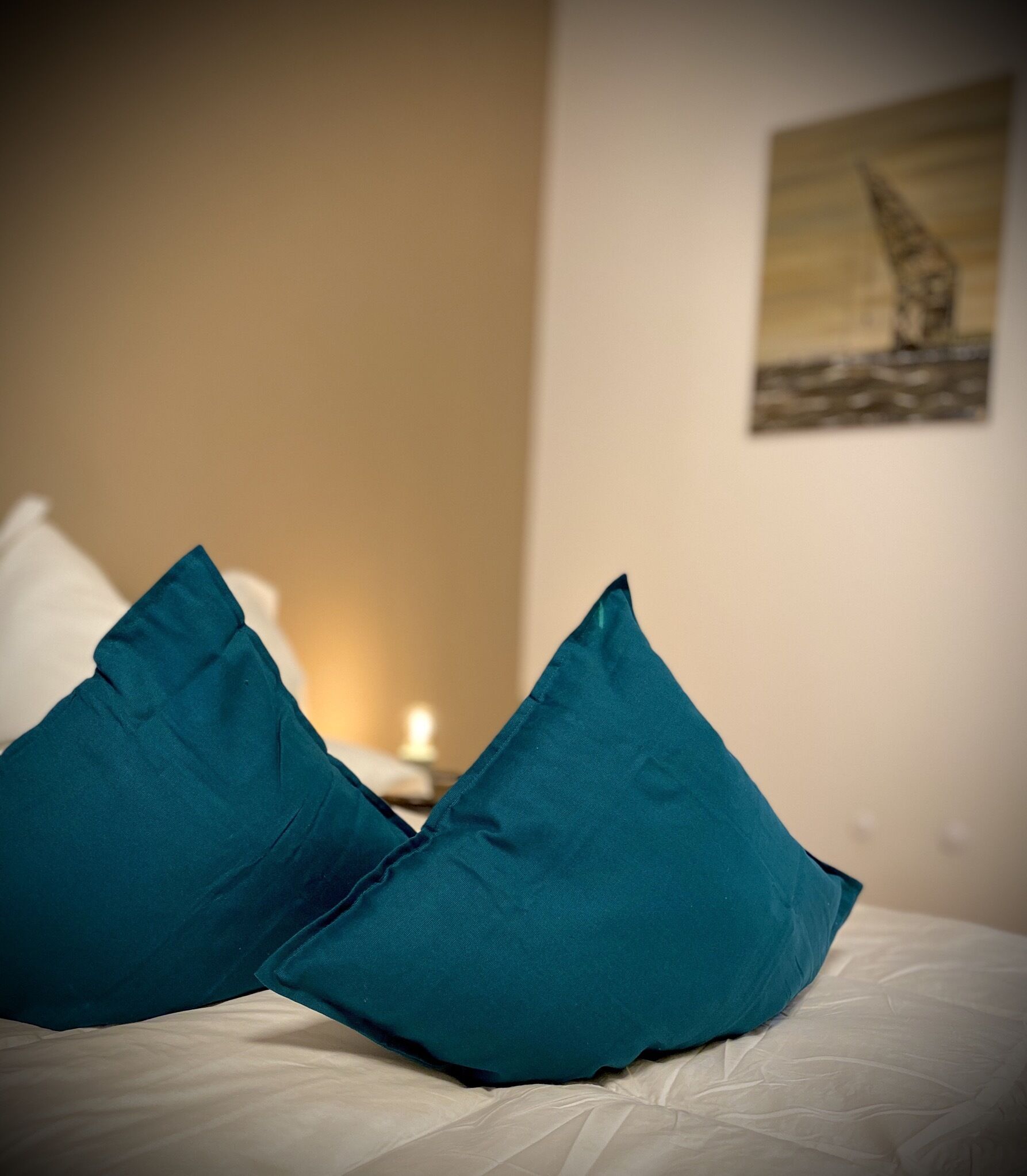 A bed with teal pillows and a painting on the wall.
