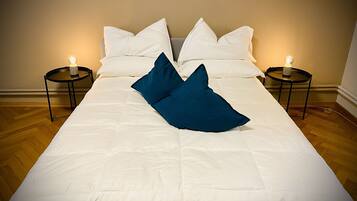 A neatly made bed with white linens and two blue pillows, flanked by two bedside tables with lit candles.
