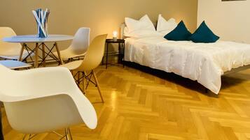 A room with a bed, white chairs, a small table with a candle, and a wooden parquet floor.