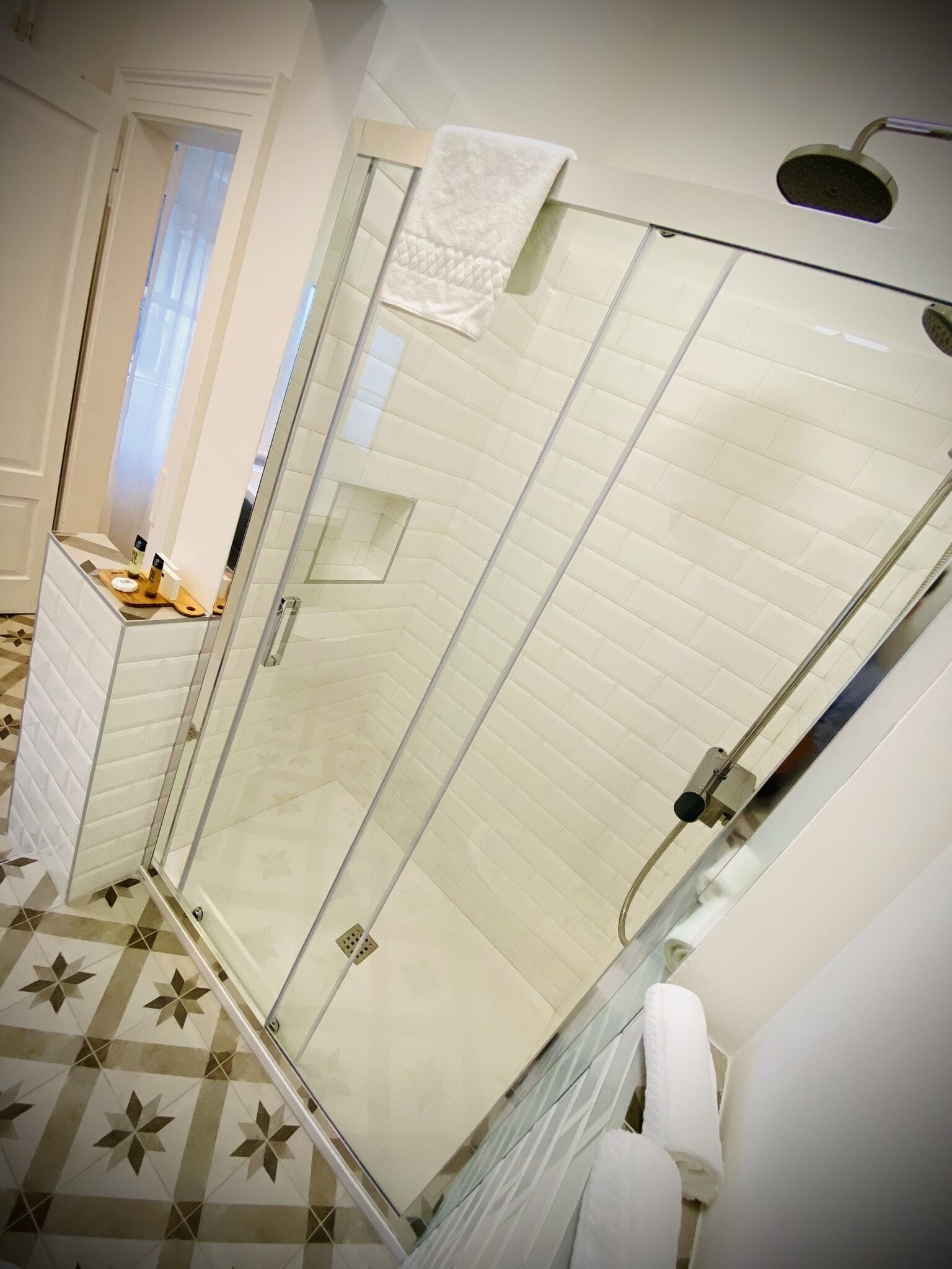 A modern bathroom with a glass-enclosed shower, white tiles, and a patterned floor.