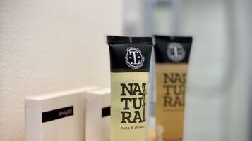 Dos tubos de gel de ducha y baño 'NATURAL' sobre una bandeja de madera, con una caja de 'Sewing Kit' a su lado.