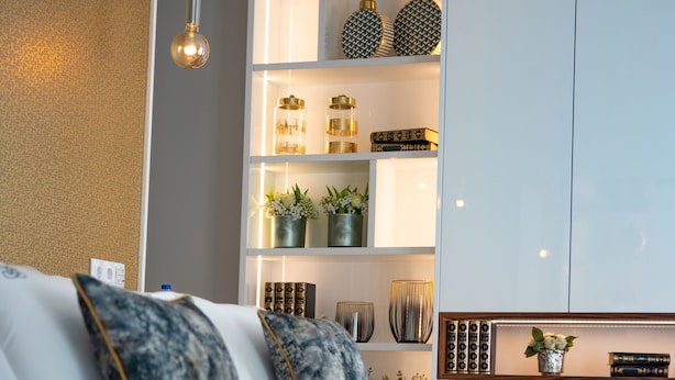 Una sala de estar moderna con un sofá, un lámpara colgante y una estantería empotrada decorada con objetos.