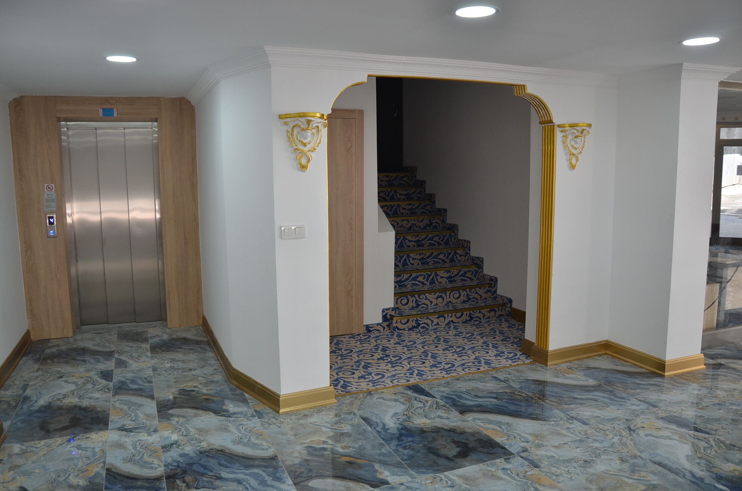 A hallway with a marble floor, an elevator, and a staircase with patterned carpet.