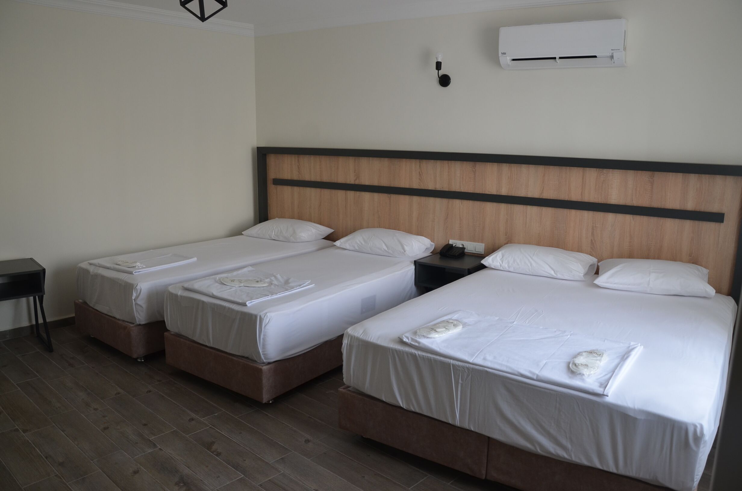 A hotel room with two single beds, a bedside table, a nightstand, and a wall-mounted air conditioner.