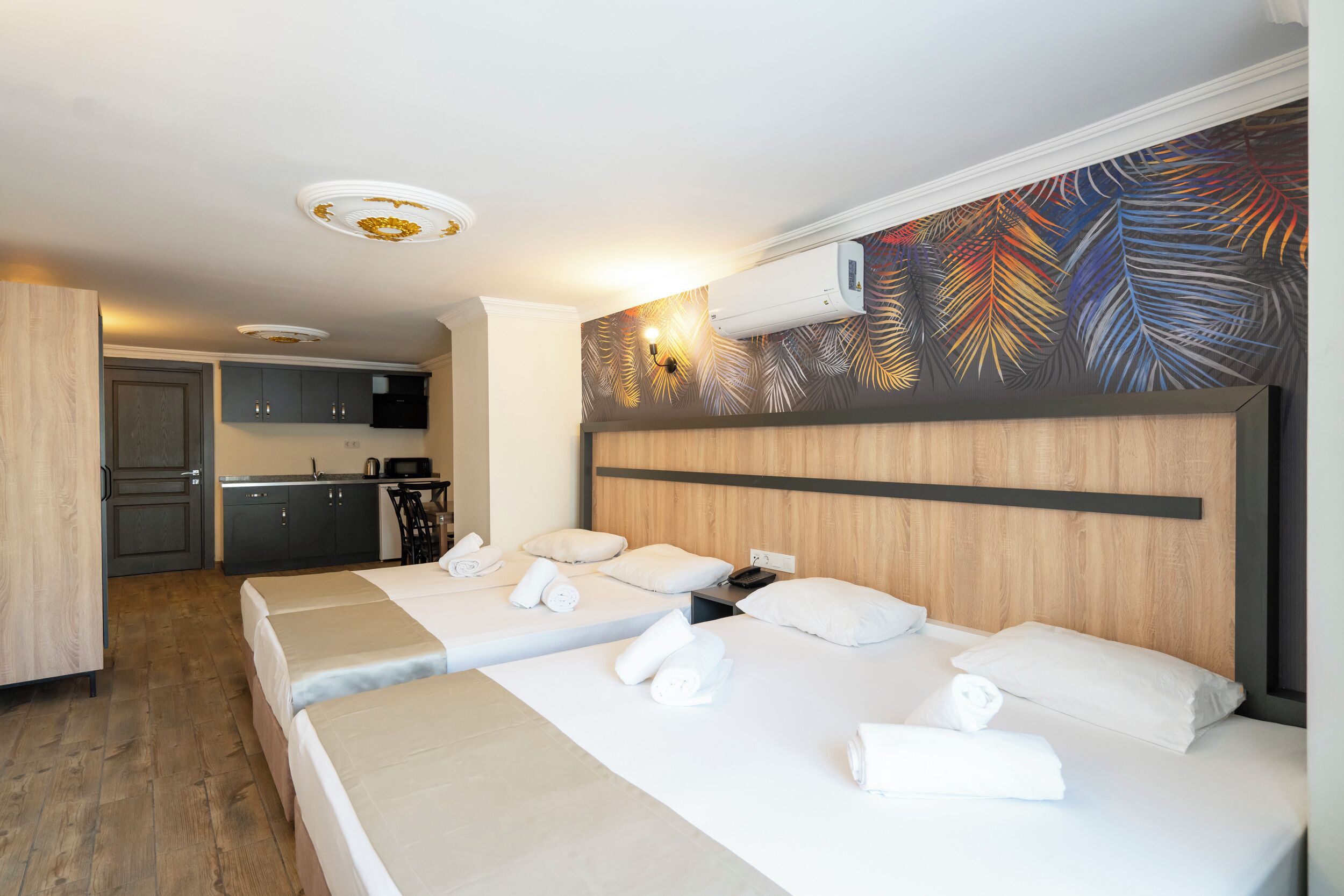 A hotel room with two beds, a kitchenette, and a bathroom.