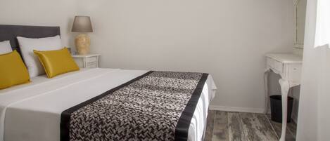 Una cama bien hecha con un edredón estampado, una lámpara de noche y un televisor montado en la pared.