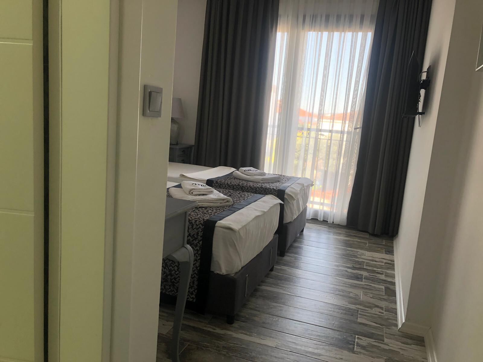 Habitación de hotel con dos camas, piso de madera, ventana con cortinas y una puerta.