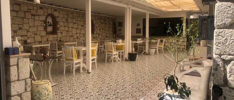 An outdoor patio area with stone walls, patterned flooring, and white furniture.
