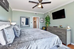 A bedroom with a bed, a ceiling fan, a TV, and a dresser.