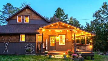 A wooden house with a porch, a welcome sign, and a wheelbarrow.