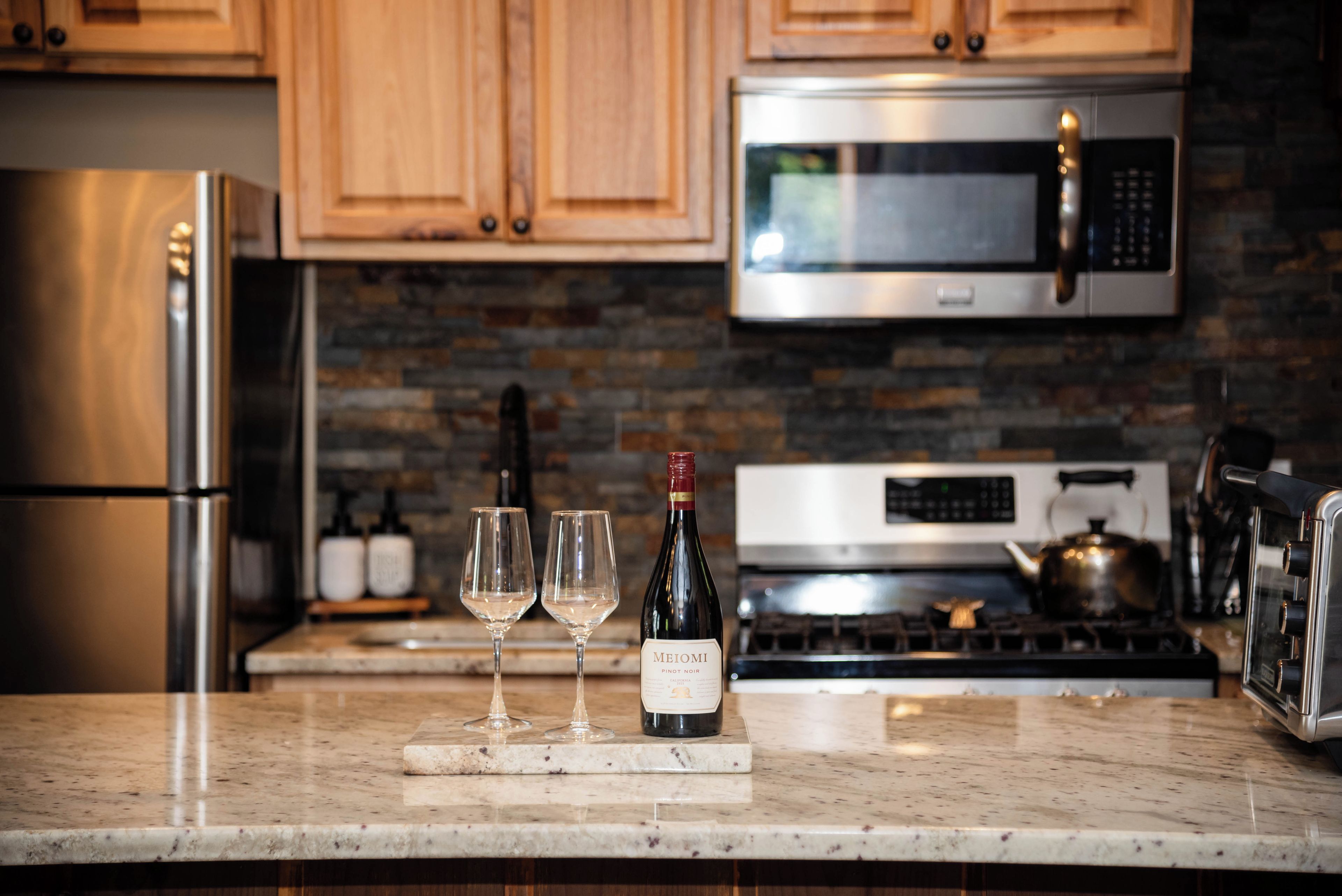 A kitchen with wooden cabinets, a stainless steel refrigerator, a microwave, and a stove.