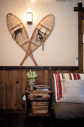 Un porte-planches fixé au mur, avec deux planches de surf, une petite table avec une plante et un lit avec des oreillers à rayures.