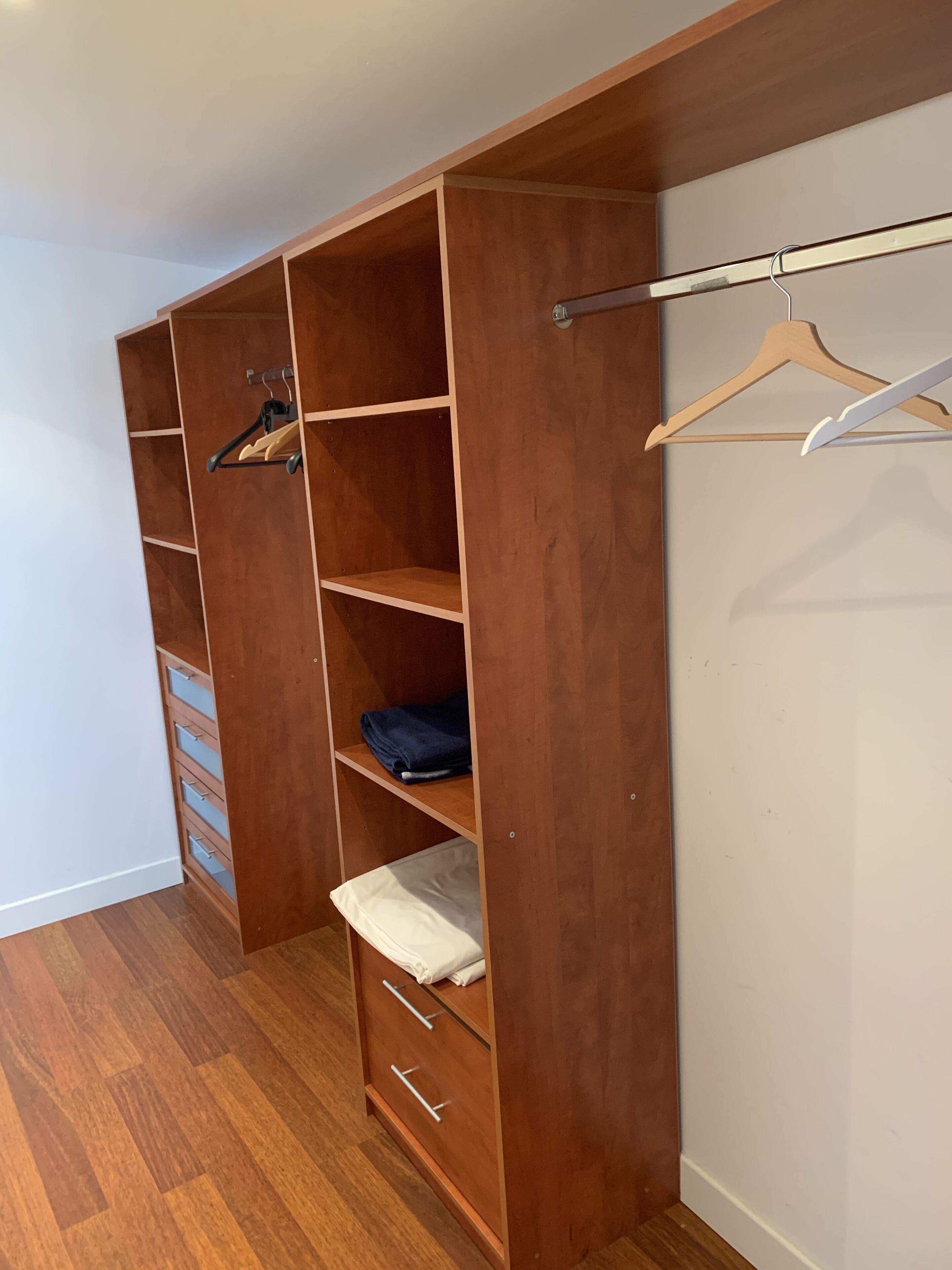 Een inloopkast met houten planken, een kledingroede en lades.
