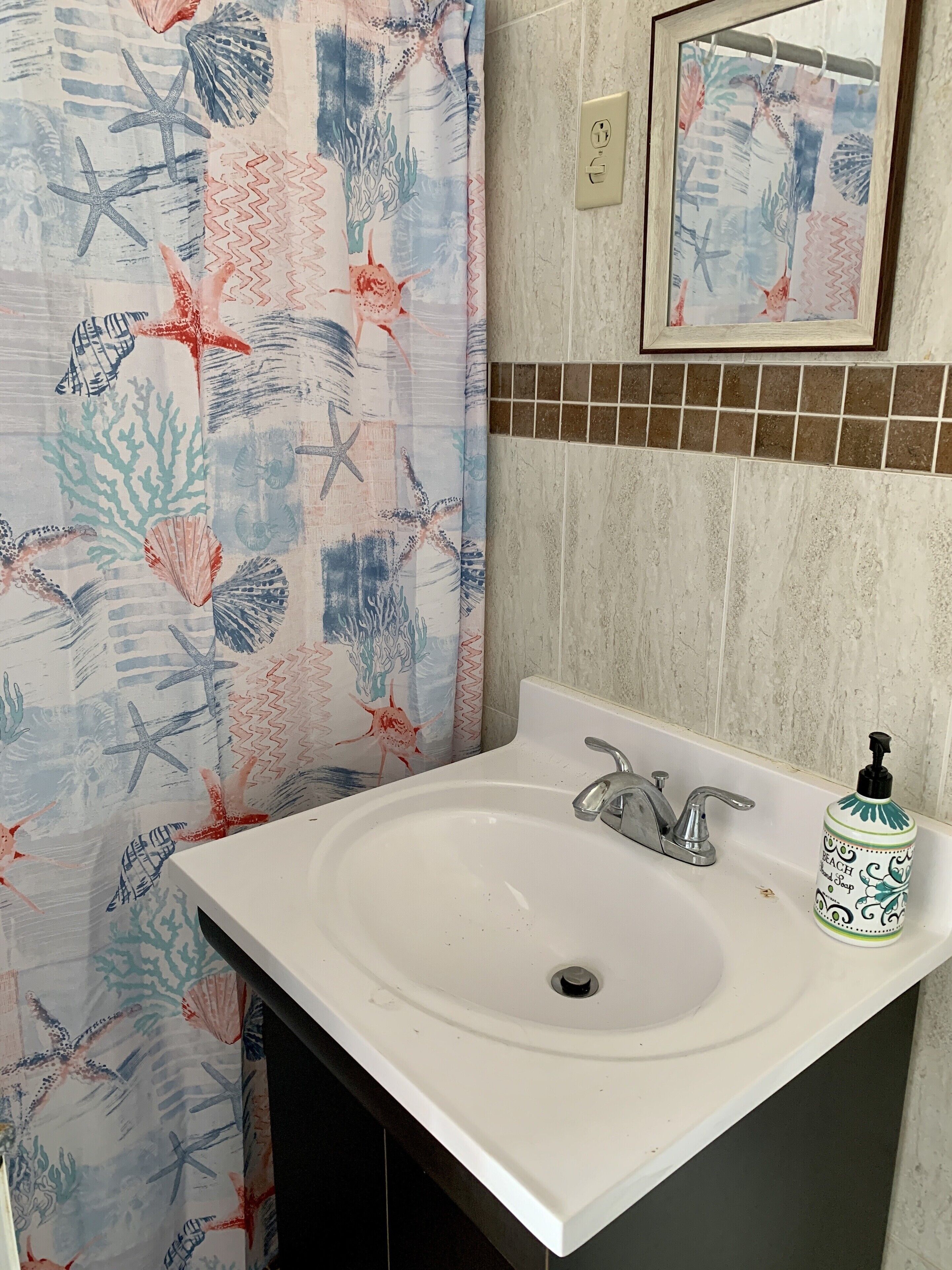 A bathroom with a white sink, a mirror above it, and a shower curtain with a sea-themed pattern.