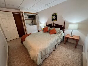 A bedroom with a bed, a nightstand with a lamp, a closet with a hanging rack, and a door. - Cozy lake front unit close to Honesdale, Elk Mountain, Scranton & much more! (Waymart)