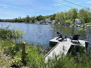Un muelle con dos sillas Adirondack, un letrero de privacidad y un lago tranquilo con casas al fondo.