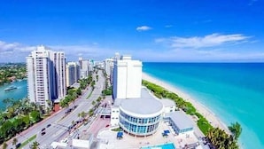 A coastal cityscape with high-rise buildings, a beachfront, and a round building with a blue roof.