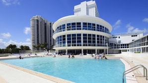 A modern hotel with a circular pool area, surrounded by palm trees and a clear blue sky.