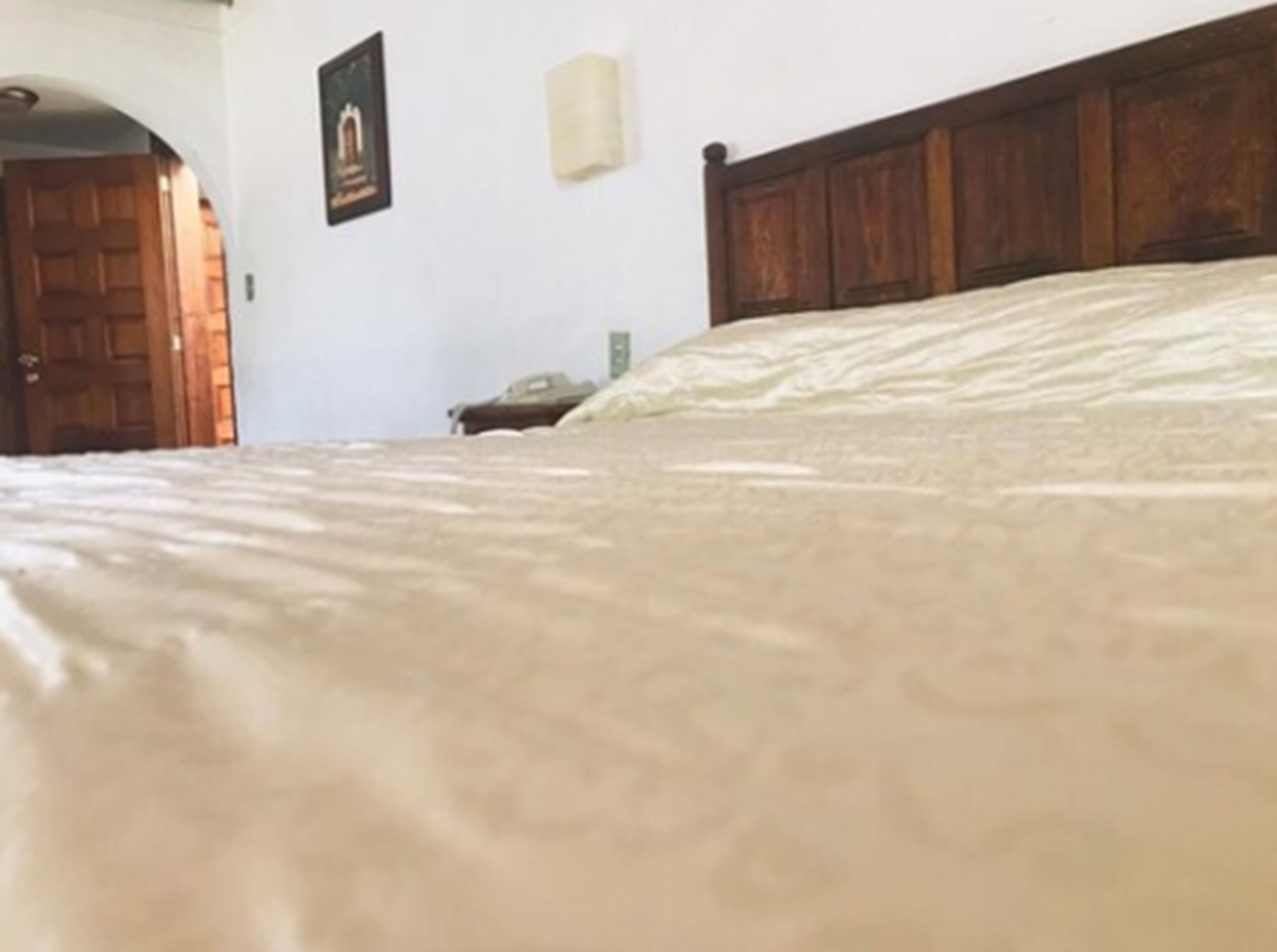 Een slaapkamer met een houten hoofdbord, een bed met een beige dekbedovertrek, een ingelijst beeld aan de muur en een houten deur op de achtergrond.