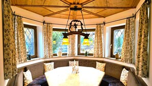 Una habitación acogedora con una mesa redonda y bancos, ventanas amplias con cortinas y techo de madera.