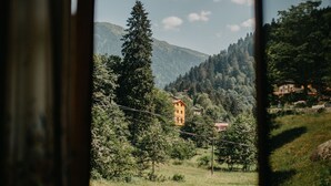 Vista a través de una ventana mostrando un paisaje montañoso con un edificio y árboles.