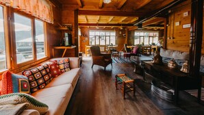 Un interior de cabaña acogedor, con piso de madera, un sofá con mantas coloridas, un comedor y una chimenea.