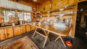 Una cocina rústica de madera con una gran mesa de madera, una cafetera y estantes con cristalería.