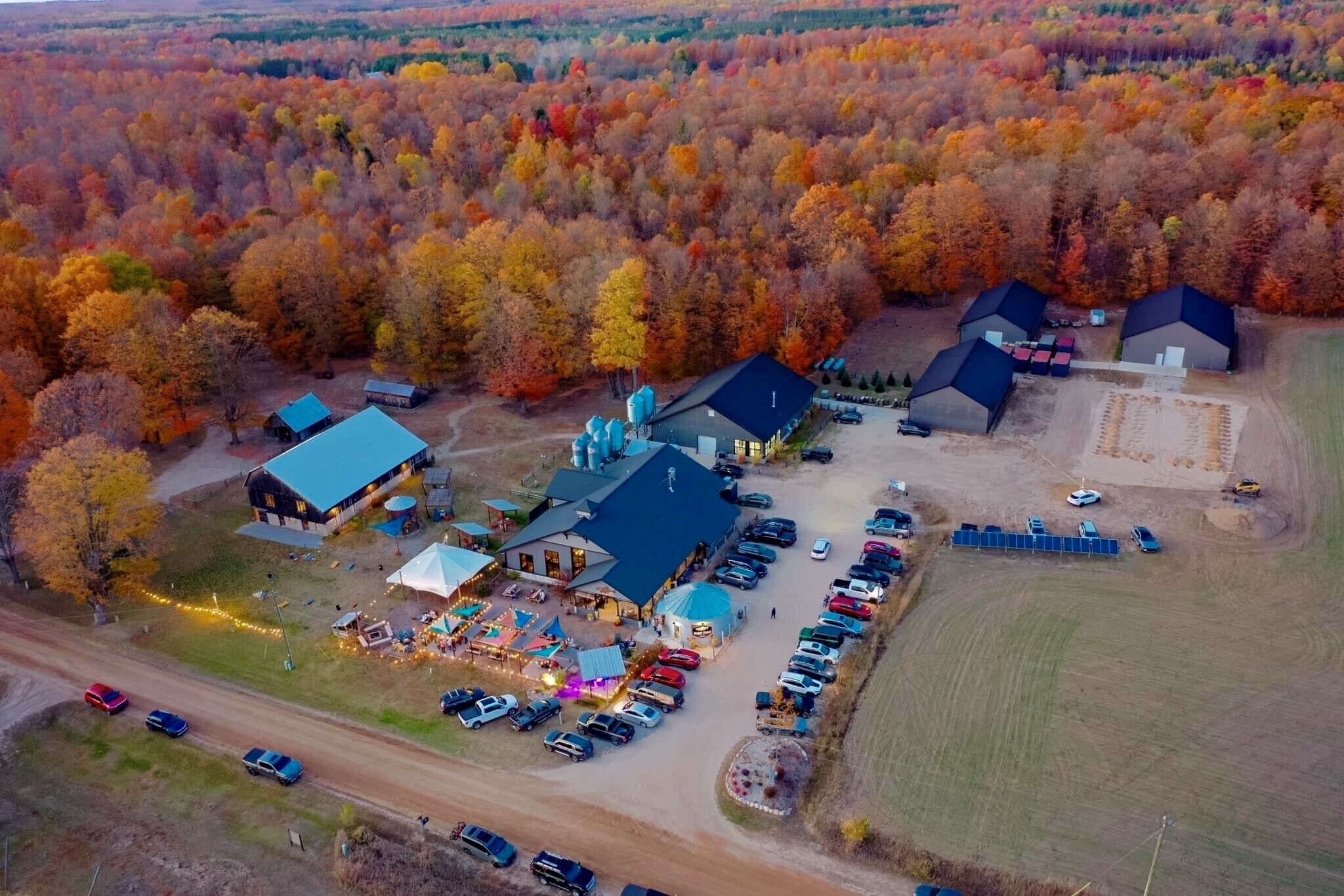 Une vue aérienne d’un terrain de camping comprenant plusieurs cabanes, un bâtiment central doté d’un toit bleu et un espace de stationnement avec plusieurs voitures.