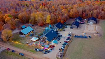 Une vue aérienne d’un terrain de camping comprenant plusieurs cabanes, un bâtiment central doté d’un toit bleu et un espace de stationnement avec plusieurs voitures.